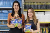 Foto mostra duas mulheres segurando cartilhas educativas do programa TRT na Escola