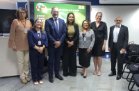 Foto mostra servidores e autoridades convidadas posicionadas de pé no auditório da Escola Judicial.