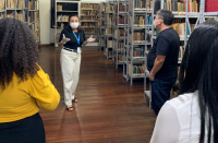 Foto mostra um grupo de pessoas acompanhando a explicação de uma funcionária sobre preservação de um acervo documental.