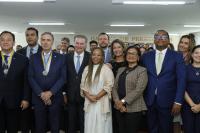 Foto mostra pessoas posicionadas de pé, dentro de um auditório. 