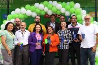 Foto mostra 11 pessoas, entre homens e mulheres. Todos de pé. Ao fundo um arco feito com balões nas cores verde e branco.
