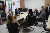 Foto mostra cinco pessoas sentadas em volta de uma mesa. São 3 homens e duas mulheres.