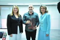 Foto mostra duas melheres ao lado de um homem. Ele segura uma sacola de papel