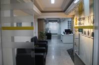 Foto mostra uma a entrada de uma sala. A esquerda tem duas poltronas. Na direita o nome Diretoria Geral. Ao fundo do corredor uma mesa de recepção. 