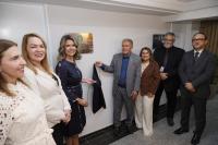 A foto mostra sete pessoas entre homens e mulheres em frente a uma placa de inauguração de um ambiente.