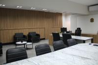 Foto mostra uma sala grande com mesa de mármore, cadeiras e poltronas e ao fundo uma mesa em formato de "L"