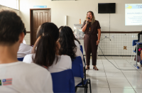Foto mostra uma mulher, em pé em uma sala de aula. Sentados de frente para a mulher, alunos e alunas do colégio IEMA.