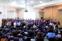 Foto mostra dezenas de pessoas, posicionadas em pé, em um palco no centro de um auditório