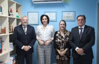 Foto mostra dois homens e duas mulheres em pé. Ao fundo uma parede azul. Na esquerda uma esquerda.