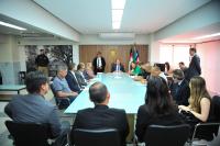 Foto mostra um grupo de pessoas sentados em volta de uma mesa de reunião. 