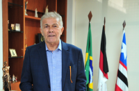 Foto mostra um homem em pé no primeiro plano. Ao fundo bandeiras do Brasil, da Justiça do Trabalho e do Maranhão foram posicionadas.