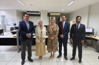 Foto mostra duas mulheres e três homens. Ambos estão em pé no meio de uma sala.