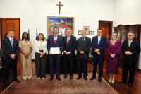 Foto mostra um grupo de pessoas em pé. No centro um homem segura um certificado