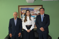 Foto mostra dois homens e uma mulher. Eles estão em pé, lado a lado. Ao fundo uma parede verde e um quadro colorido