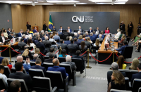 Foto mostra várias pessoas sentadas em um auditório. Ao fundo a logomarca do Conselho Nacional de Justiça.