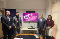 Foto mostra 3 homens e uma mulher. Todos estão em pé na frente de um monitor de tv com a informação audiência pública