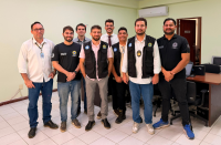 Foto mostra um grupo de pessoas. Todos estão em pé no meio de uma sala