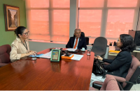Foto mostra um homem e duas mulheres sentados à mesa. 