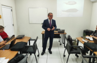 Foto mostra um homem usando um terno escuro, posicionado em pé no meio de uma sala de treinamento