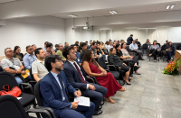 Foto mostra várias pessoas sentadas dentro de um auditório
