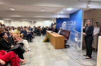 Foto mostra uma mulher em pé falando para pessoas em um auditório
