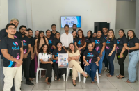Várias pessoas reunidas em uma sala. Algumas estão em pé. Ao centro uma pessoa segura um cartaz com a informação do PID.