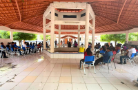 Foto mostra pessoas reunidas no pátio de um terraço. Alguns estão em pé e a maioria das pessoas estão sentadas.