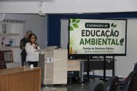 Foto mostra uma mulher em pé, falando ao microfome. Ao lado um painel: II Seminário Educação Ambiental