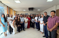 Foto mostra várias pessoas em pé, uma ao lado da outra dentro de uma sala.