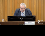 Imagem com fundo em madeira, ao centro o presidente do TST, Ministro Emmanoel Pereira, sentado em bancada do Plenário do TST, tendo a sua frente uma tela de computador, microfones, à frente da bancada placa com seu nome e cargo, e ao lado logomarca do TST