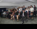 Imagem de grupo de magistradas e magistrados sentados e de pé formando fileiras no auditório da Escola Judicial, sendo possível ver o teto branco e piso em granito cinza.