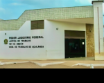 Foto da fachada principal da Vara do Trabalho de Açailândia, localizada no Sul do Maranhão, no primeiro plano uma parede branca com o brasão do Poder Judiciário e ao lado está escrito o Poder Judiciário Federal, Justiça do Trabalho, TRT-16ª Região, Vara do Trabalho de Açailândia, ao lado uma porta de vidro escura e demais partes da fachada na cor bege com tons de caramelo