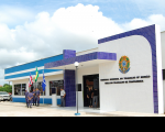 Foto da fachada principal da sede da Vara do Trabalho de Chapadinha. A fachada pintada nas cores azul celeste e branca, com detalhes em cerâmica azul marinho. Portas e janelas de vidro transparente. Na frente da fachada, policiais e um vigilantes e mais duas pessoas. Também estão hasteadas as bandeiras do Brasil, Maranhã e de Chapadinha. Na parede principal da fachada há um brasão e abaixo está escrito: Tribunal Regional do Trabalho da 16ª Região - Vara do Trabalho de Chapadinha