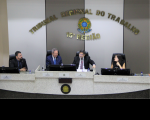 Três homens e uma mulher sentados à mesa do Plenário, à frente de parede listrada de branco e marrom com a inscrição Tribunal Regional do Trabalho 16ª Região em dourado e brasão da República.