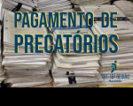Foto de processos físicos empilhados. Em primeiro plano, ao centro, a inscrição PAGAMENTO DE PRECATÓRIOS em azul com sombra amarela e, no canto inferior direito, a logomarca do TRT-16 na versão colorida.
