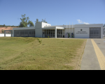 Foto da sede da Vara do Trabalho de Caxias. No primeiro plano, vê-se o gramado. Ao fundo, a fachada principal da sede da VT pintada na cor branca. À direita, mastros com as bandeiras do Brasil, Maranhão e Caxias. Ao lado, uma parede branca com o brasão do Poder Judiciário e abaixo está escrito: Justiça do Trabalho, Vara do Trabalho de Caxias. Portas de vidros e portas e janelas com persianas claras. Por trás da sede, vê-se copas de arvores.