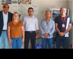 Foto de uma mulher e quatro homens em pé, à frente de parede bege decorada com fotos e diplomas
