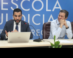 Juiz Sergei Becker ao lado do professor Ricardo Festi na mesa de abertura da Semana. O juiz veste terno escuro e o professor camisa de manga comprida azul. 