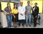Foto de pessoas (homens e mulheres) em pé, em um auditório, ao fundo um aparelho de TV e um telão com informações sobre palestra referente ao Setembro Amarelo