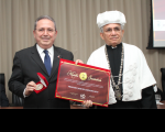 Foto do desembargador Carvalho Neto, de terno escuro e seguranda a medalha e o diploma entregues pelo reitor da Natalino Salgado, à sua esquerda.