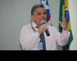 Foto de um homem falando ao microfone. Ao fundo, as bandeiras do Brasil e do Maranhão.
