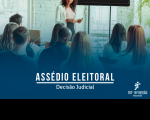 Grupo de pessoas reunidas em uma sala de reunião branca com janelas e plantas nos cantos. Estão de costas e sentados em cadeiras de madeira olhando a palestrante