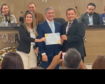 Foto de mulheres e homens (sentados e em pé), dos quais uma mulher e dois homens em pé, em primeiro plano