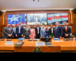 mesa de plenário com 11 pessoas reunidas para a foto. Ao fundo, painel com imagens da bandeira do maranhão 