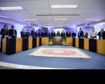 mesa de honra em plenário composto por autoridades. ao meio, tapete vermelho em piso de carpete azul