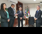 Quatro pessoas reunidas em gabinete, sendo três homens e uma mulher, atentos à leitura de termo de posse.