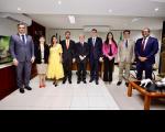 três mulheres e seis homens posam para a foto. Compõem a imagem uma mesa de centro e uma televisão na lateral esquerda. 
