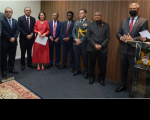 Sete homens usando ternos escuros, sendo um militar, e uma mulher de vestido que estão em pé e lado a lado.