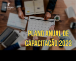 Foto de um calendário sobre uma mesa. Em volta dele, mãos de dois homens e uma mulher em atividade de análise das datas. No canto inferior direito, o texto PLANO ANUAL DE CAPACITAÇÃO 2023 em amarelo.
