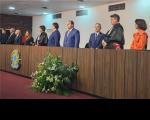 mesa de honra com 10 pessoas em pé próximas a ela. Arranjo de flores na frente da mesa de forma centralizada. Ao fundo, uma parede de cor branca.